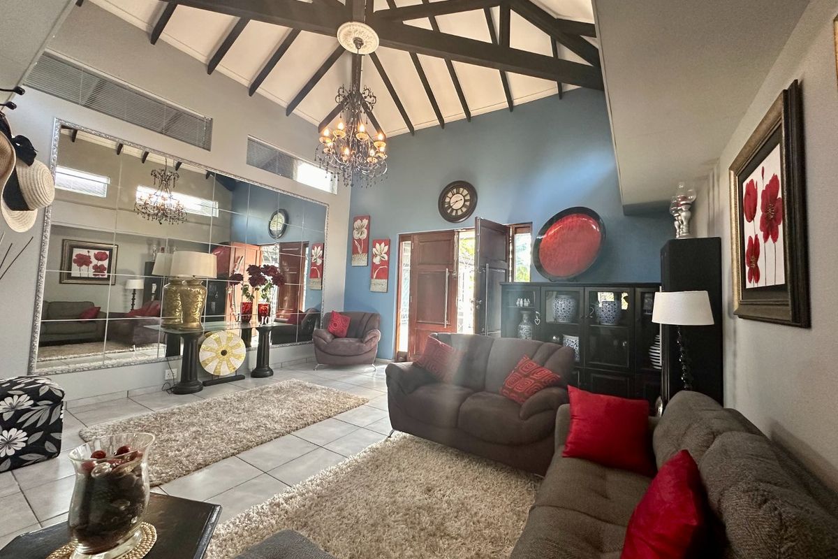 Spacious living room featuring a high vaulted ceiling with exposed timber beams, tiled flooring, and a large decorative mirrored wall.