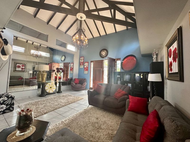 Spacious living room featuring a high vaulted ceiling with exposed timber beams, tiled flooring, and a large decorative mirrored wall.