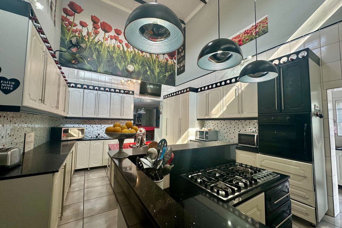 Spacious kitchen featuring contrasting black and white cabinetry, granite countertops, a built-in gas hob, and high ceilings with pendant lighting.