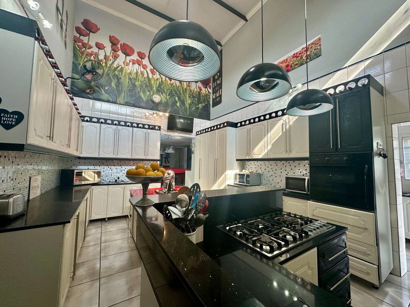 Spacious kitchen featuring contrasting black and white cabinetry, granite countertops, a built-in gas hob, and high ceilings with pendant lighting.