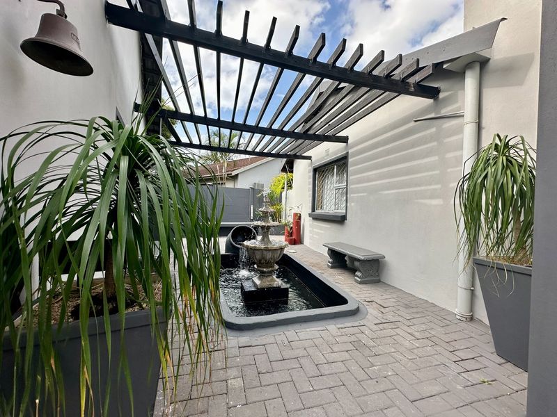 A well-maintained outdoor patio area featuring a pergola, paved flooring, and a central water feature, providing a tranquil space for relaxation.