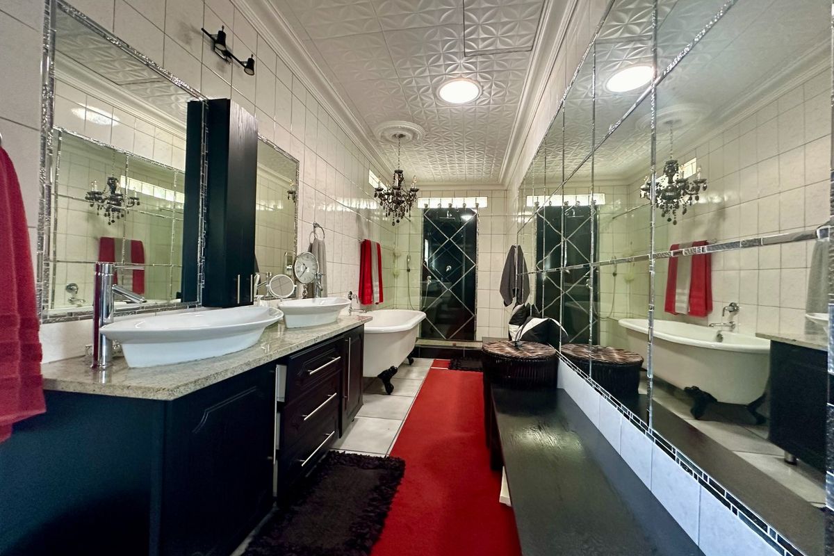 A spacious bathroom featuring a double vanity with vessel sinks, a classic clawfoot bathtub, extensive wall mirrors, and decorative patterned ceiling tiles.