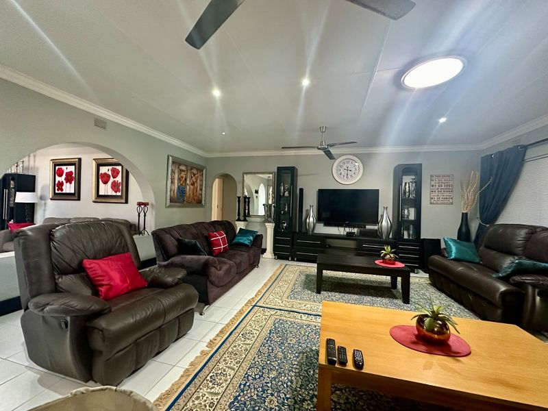 A spacious living room featuring tiled flooring, recessed lighting, ceiling fans, and an architectural archway leading to adjacent living spaces.