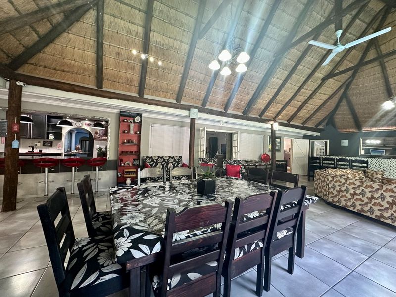 Spacious open-plan living and dining area featuring a high vaulted thatched roof with exposed timber rafters, tiled flooring, and an integrated kitchen breakfast bar.