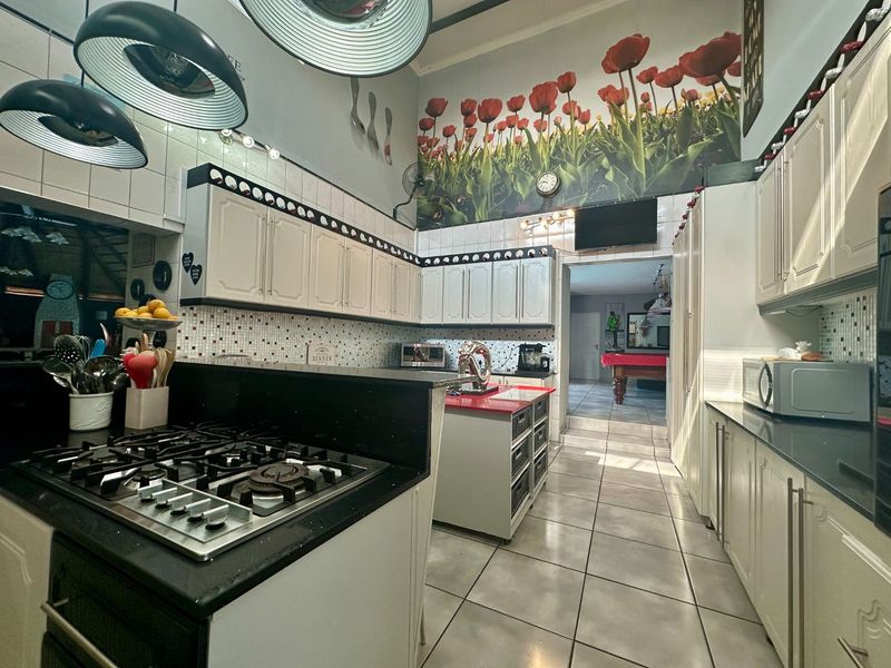 Spacious kitchen featuring white cabinetry, dark stone countertops, a gas hob, and tiled flooring with high ceilings and decorative wall mural.