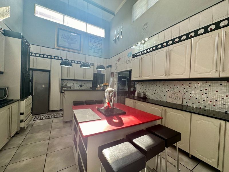 Spacious kitchen featuring a central island with a red countertop, extensive cabinetry, tiled backsplash, and high ceilings with clerestory windows for natural light.