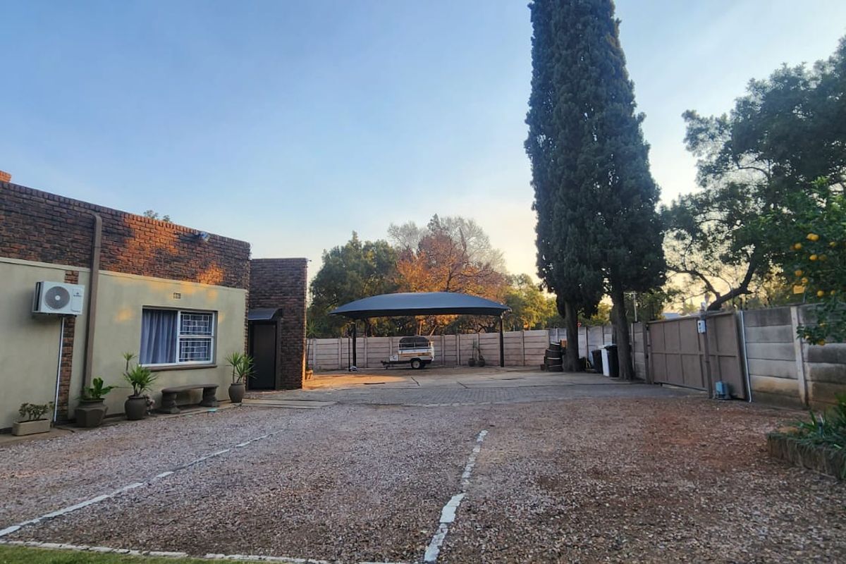 Spacious exterior area featuring a gravel driveway, paved parking section, and a covered carport structure set against a brick and plaster building facade.