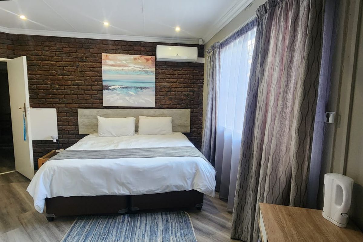A well-maintained bedroom featuring a rustic exposed brick feature wall, recessed ceiling lighting, and a wall-mounted air conditioning unit.