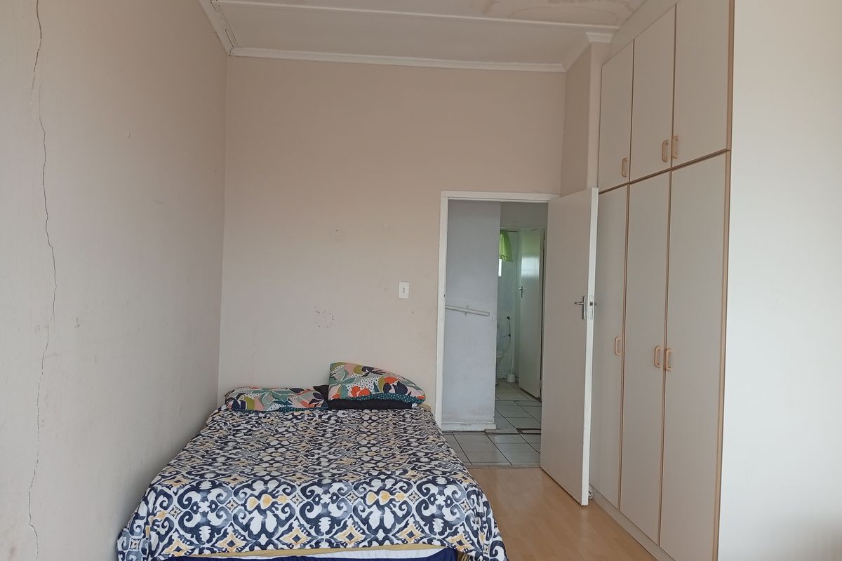 A bedroom featuring built-in cupboards and laminate flooring, showing signs of structural wall cracking and ceiling water damage.