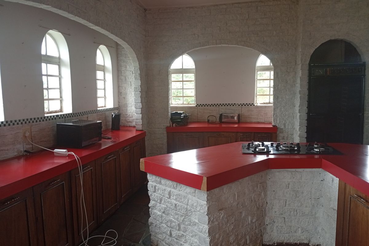 Spacious kitchen featuring white painted brick walls, arched windows, wooden cabinetry, and vibrant red countertops with a built-in gas hob.