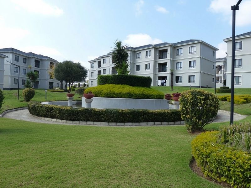 A well-maintained communal garden area featuring manicured lawns, paved walkways, and a central water feature surrounded by multi-story residential apartment blocks.