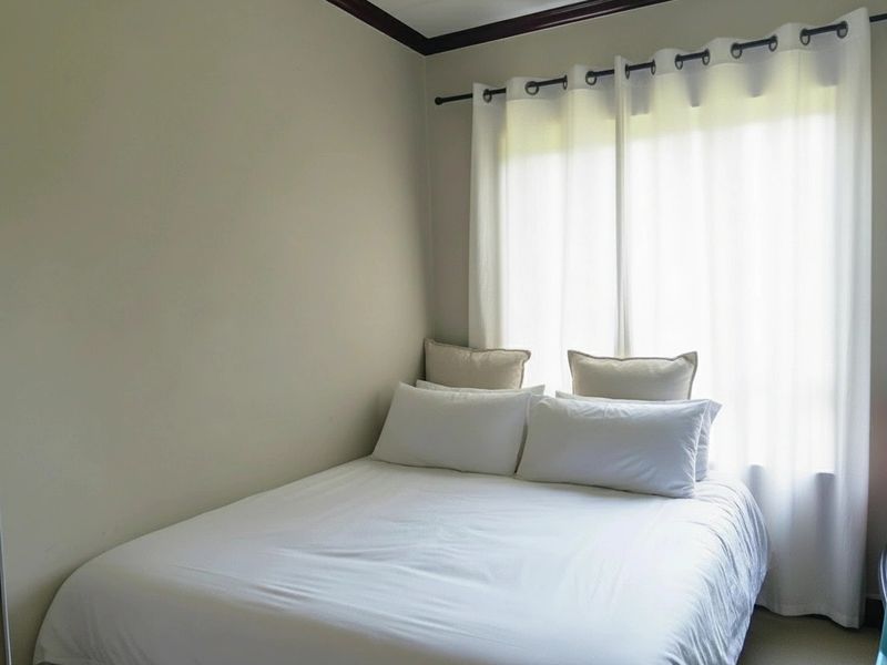 A simple bedroom featuring neutral walls, a window with fitted curtain rod, and carpeted flooring.
