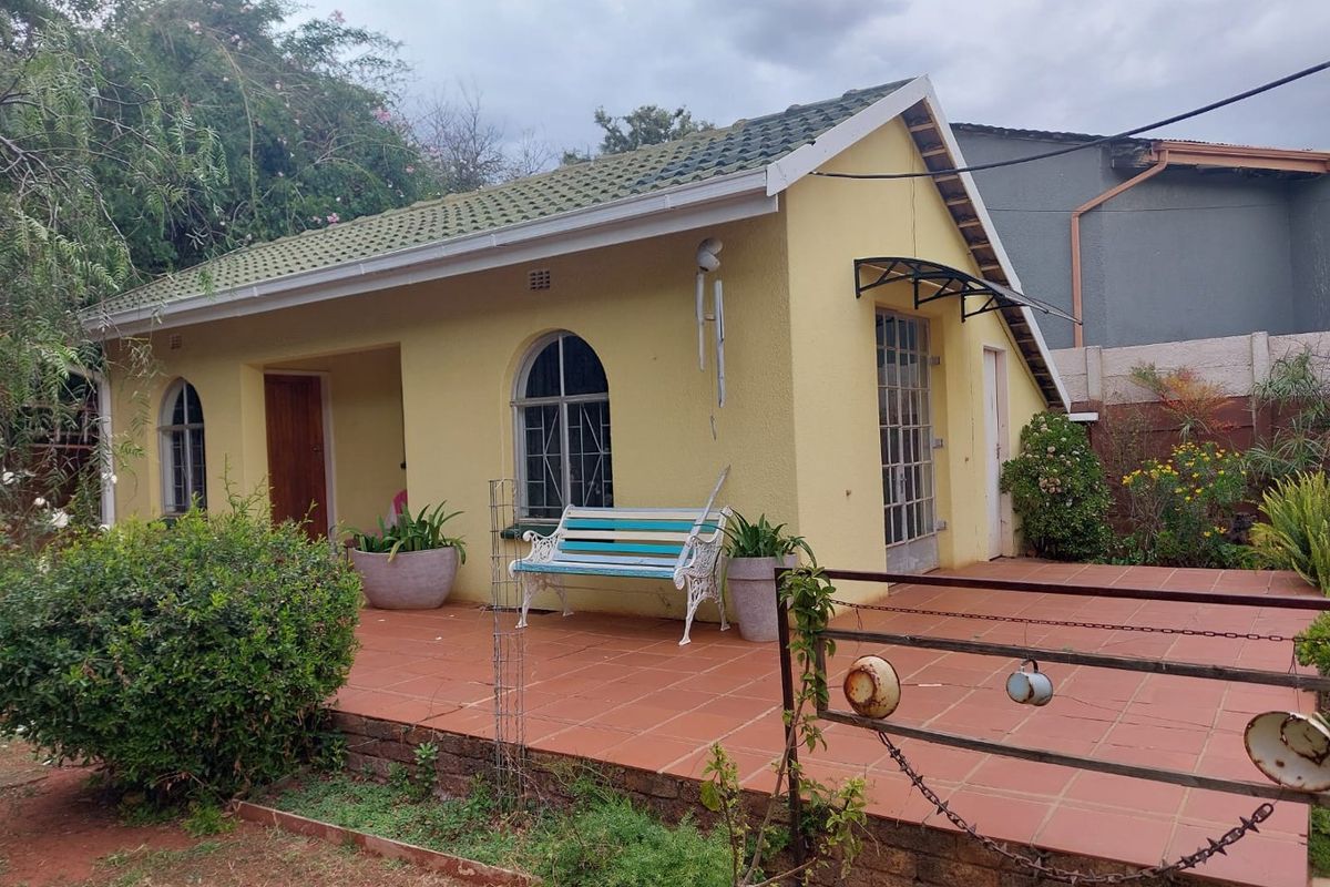 A rear view of a single-story house featuring a tiled patio, arched windows with security bars, and a tiled roof.