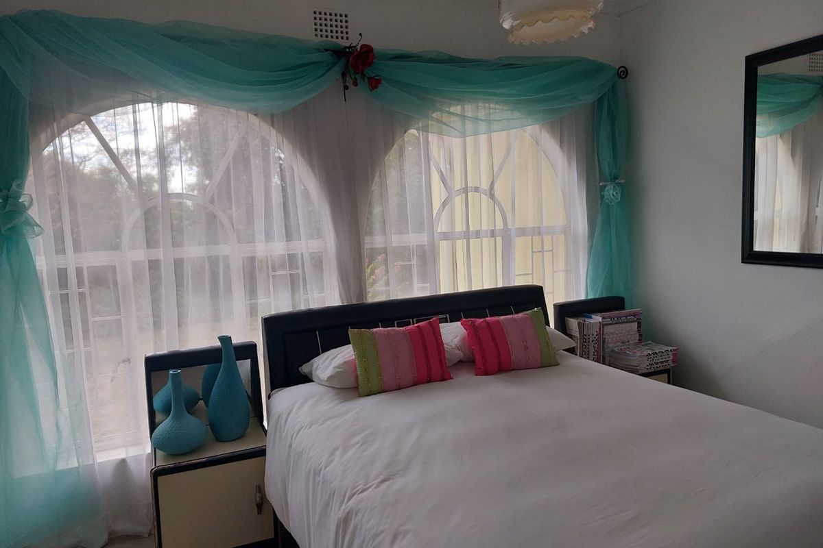 A bedroom featuring distinctive arched windows with security bars and a classic ceiling rose, offering a functional space with potential for modern updates.
