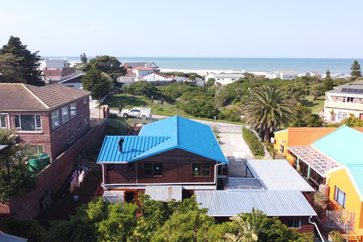 Aerial view of a coastal property featuring a blue metal roof, timber-clad exterior, and proximity to the beach.