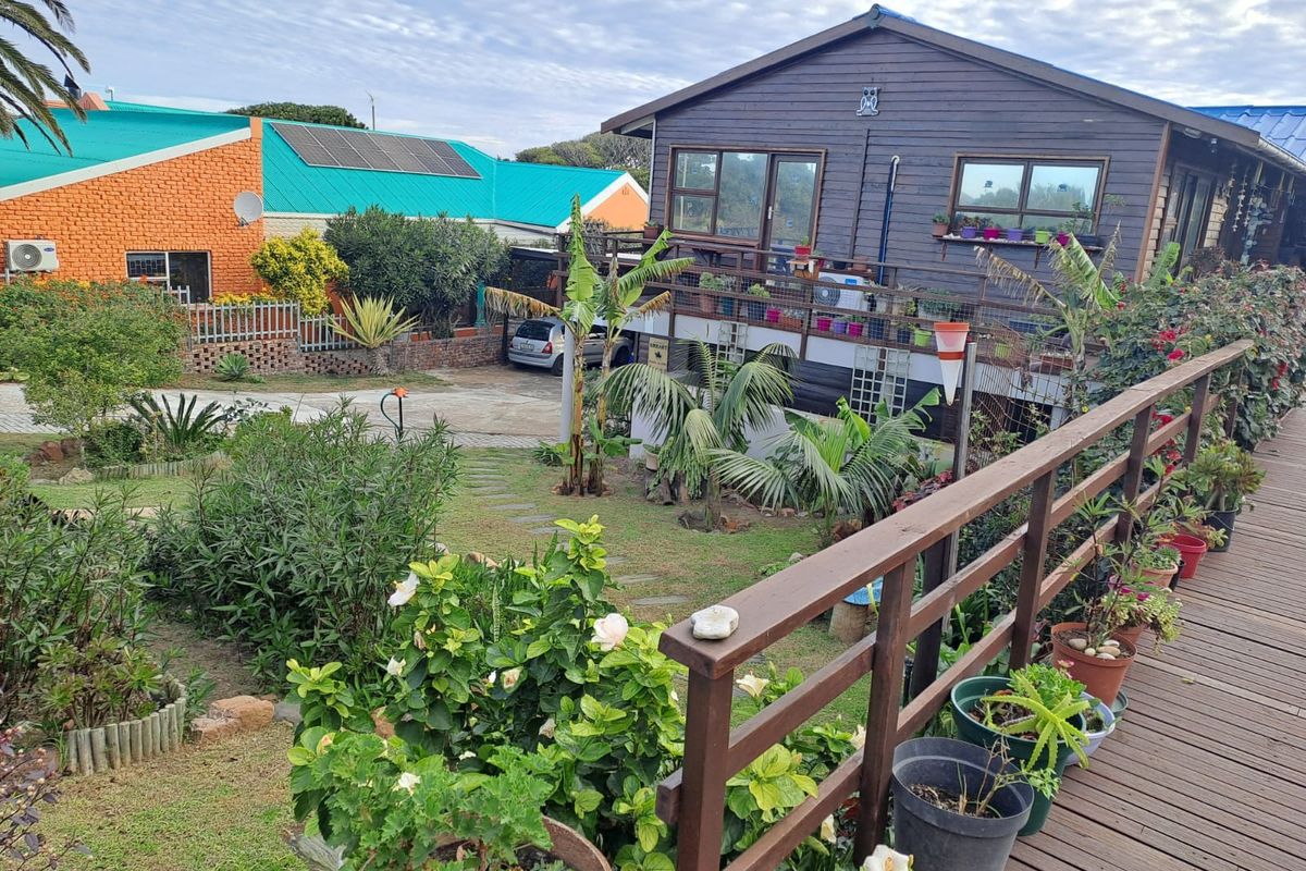 Rear view of a timber-clad house featuring a raised wooden deck, landscaped garden with stone path, and solar panels on the adjacent property.