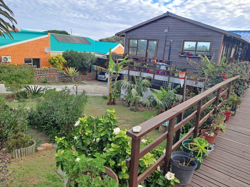 Rear view of a timber-clad house featuring a raised wooden deck, landscaped garden with stone path, and solar panels on the adjacent property.