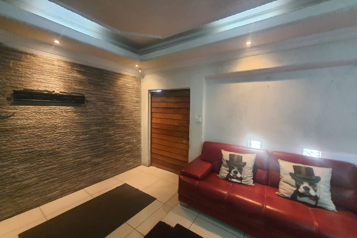 Living room featuring a textured stone feature wall, recessed tray ceiling with downlighting, tiled flooring, and a solid timber door.