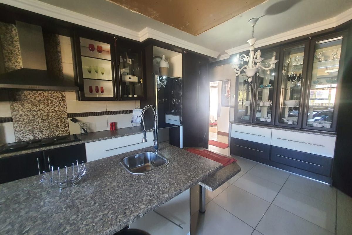 Kitchen featuring dark cabinetry, granite countertops, a central island with a sink, and built-in display cabinets, requiring minor ceiling repairs.