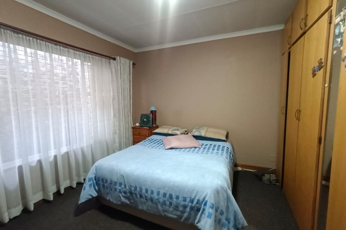 A standard bedroom featuring built-in wooden wardrobes, carpeted flooring, and large windows with curtains, offering a functional and lived-in space.
