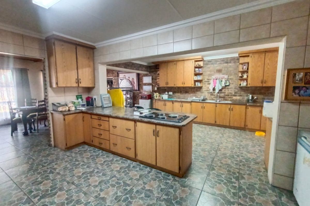 Spacious kitchen featuring wooden cabinetry, stone-look countertops, a built-in hob, and tiled flooring, offering a functional layout with ample storage space.