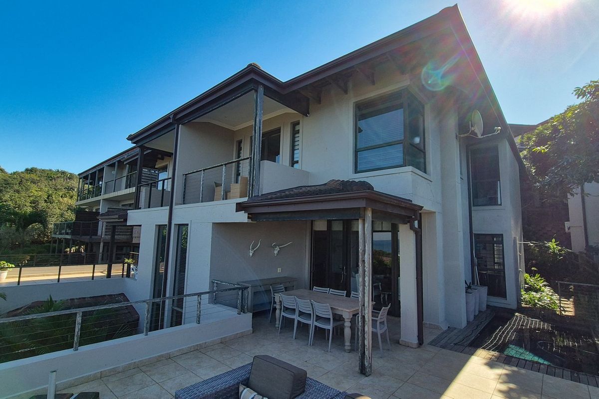 Rear view of a multi-level townhouse featuring a tiled patio, covered veranda, balcony, and established exterior finishes.