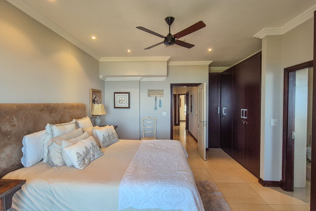 Spacious bedroom featuring built-in dark wood cupboards, tiled flooring, recessed lighting, and a ceiling fan, with an adjoining en-suite bathroom.