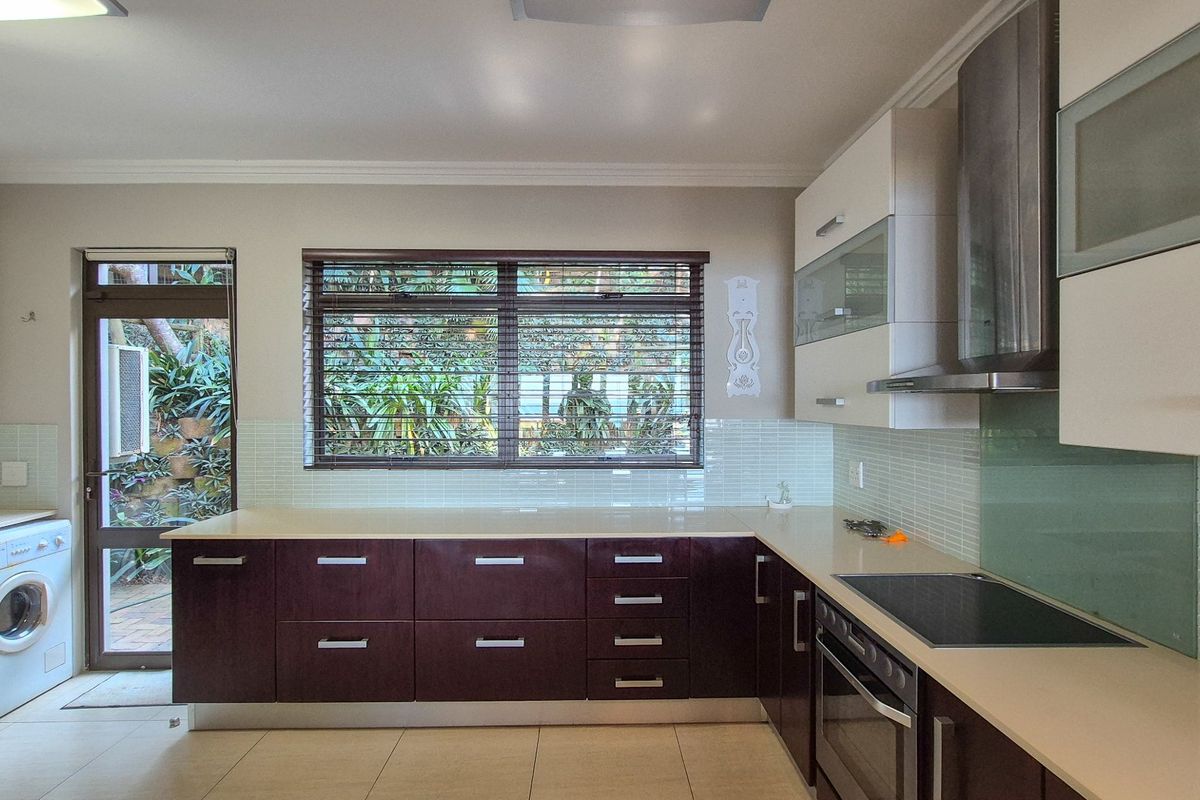 Modern kitchen featuring dark cabinetry, stone countertops, integrated appliances, tiled backsplash, and direct access to an outdoor area.