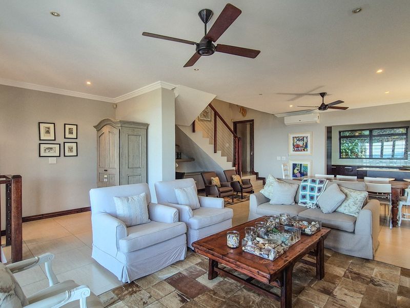 Spacious open-plan living area featuring tiled floors, ceiling fans, a central staircase, and a modern kitchen visible in the background.