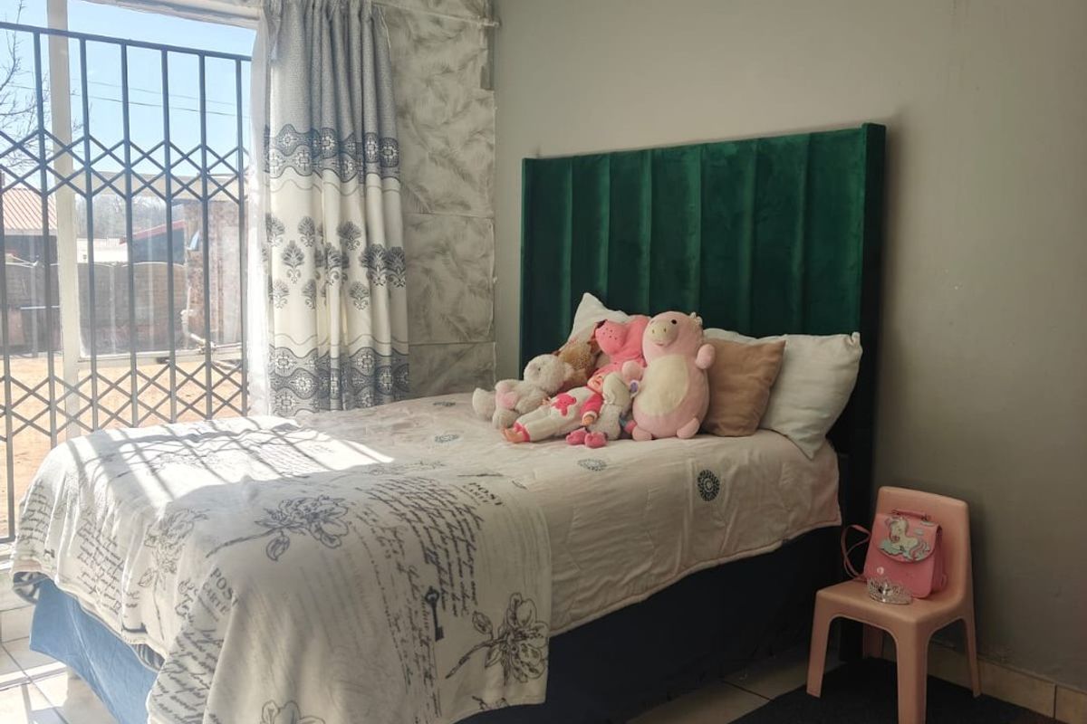 A bedroom featuring tiled flooring, a large window with security gate, and a green upholstered headboard.