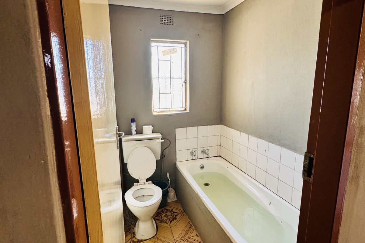 A compact bathroom featuring a standard bathtub, toilet, and tiled flooring, requiring cosmetic updates to modernize the space.