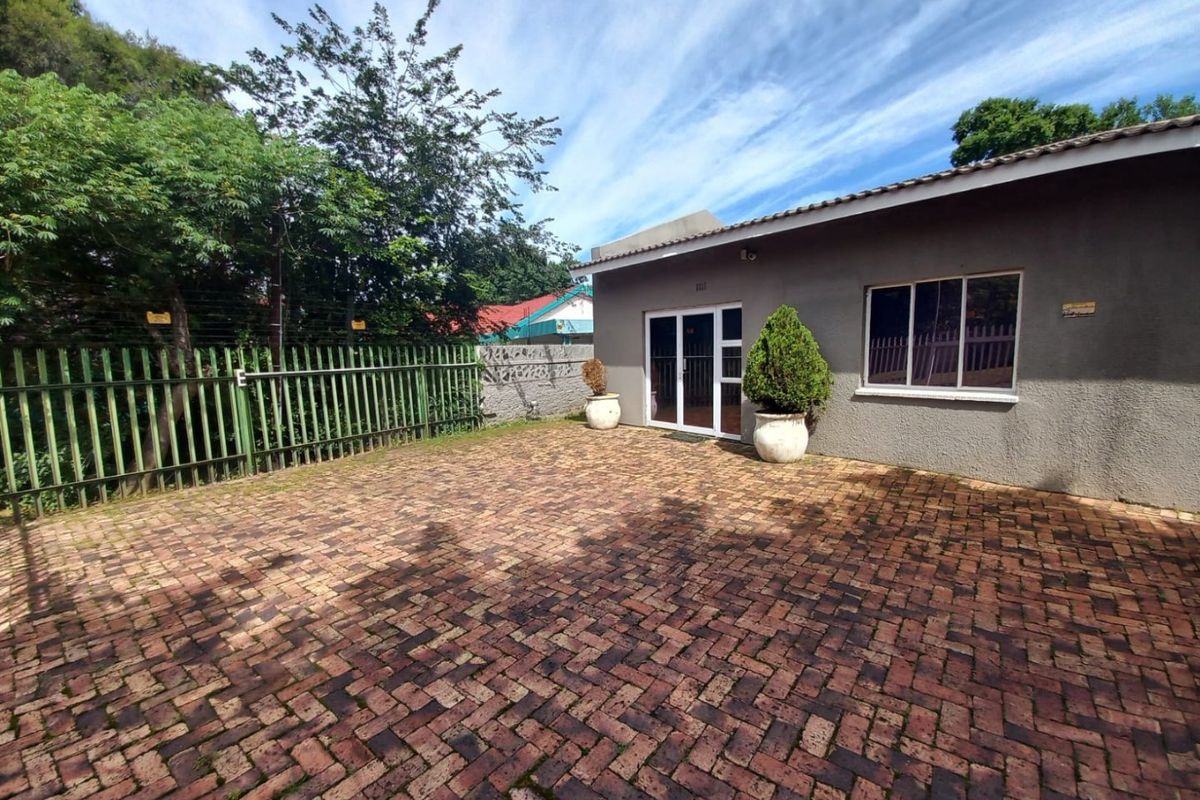 A paved rear courtyard area featuring a grey rendered exterior wall, sliding glass doors, and perimeter security fencing.