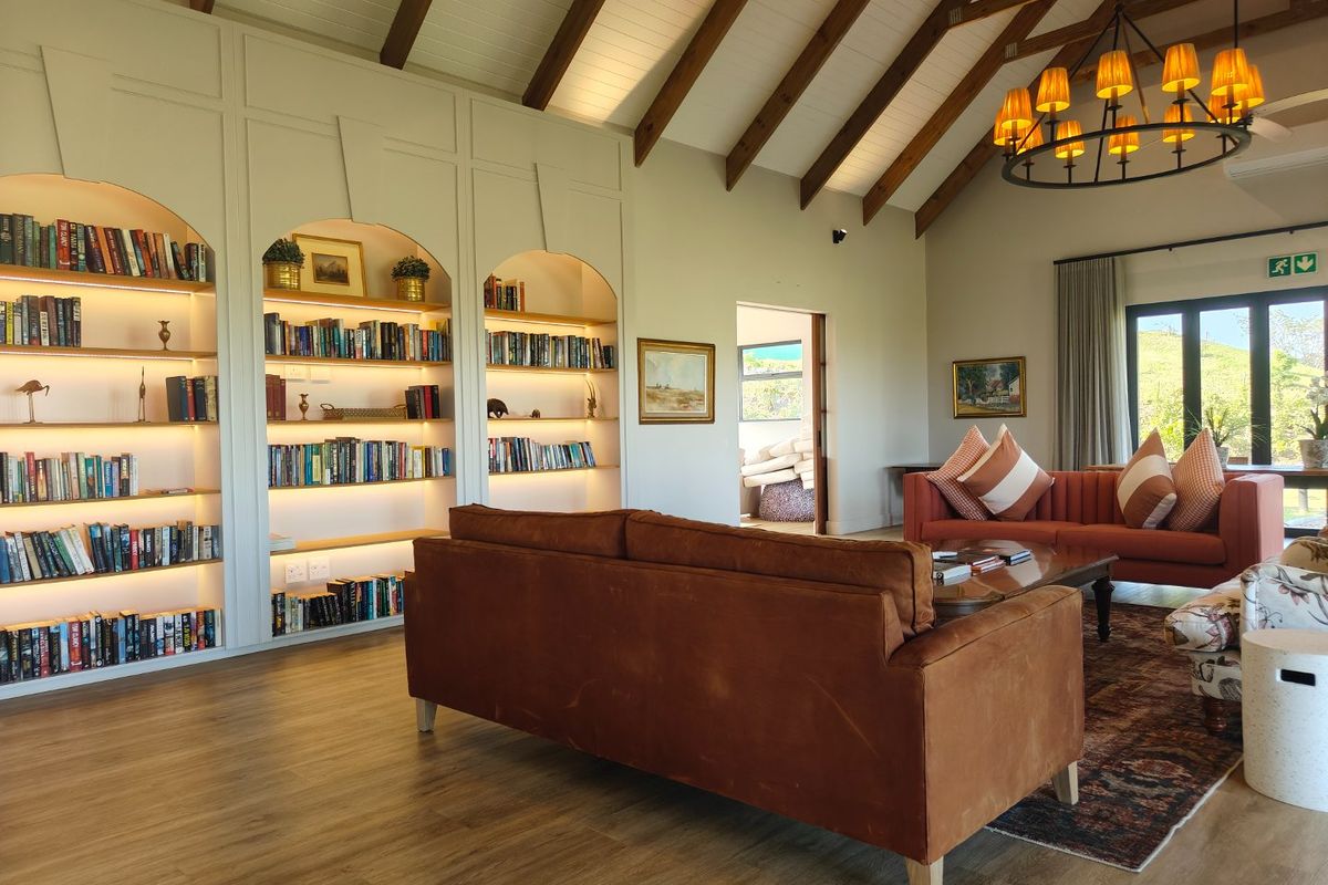 Spacious living room featuring high vaulted ceilings with exposed timber beams, custom built-in arched shelving with integrated lighting, and large windows.