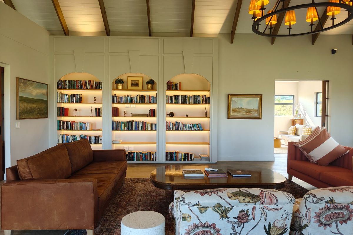 Spacious living room featuring high vaulted ceilings with exposed beams, custom built-in arched shelving with integrated lighting, and elegant chandelier lighting.