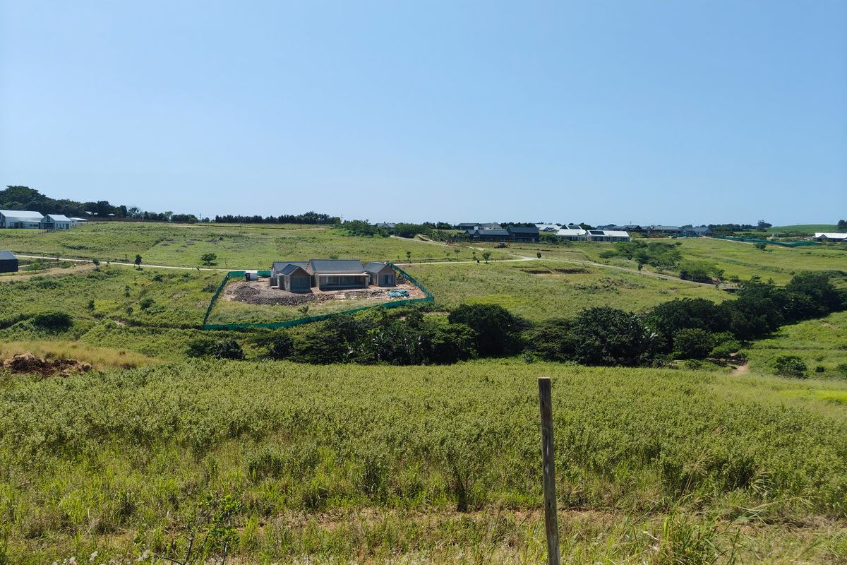 A wide-angle view of a residential vacant land plot featuring a house currently under construction in a rural estate setting.