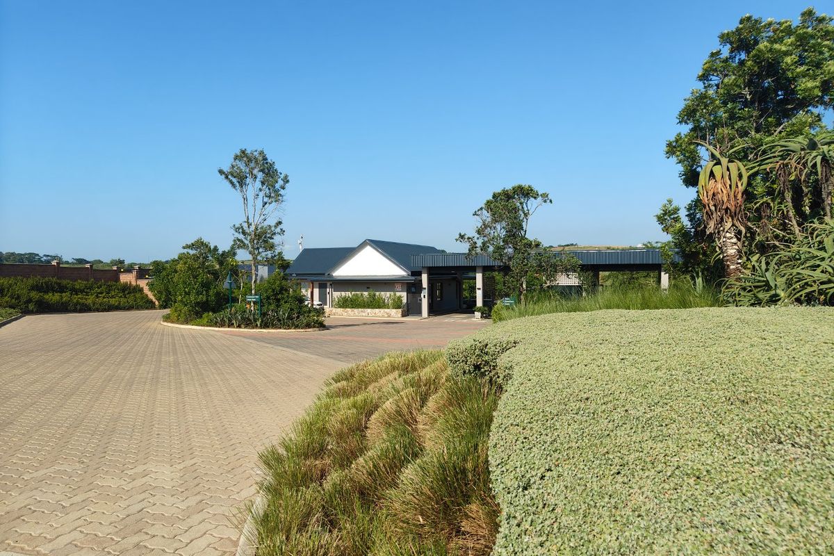 A well-maintained entrance area featuring paved driveway, landscaped garden beds, and a modern building structure with a covered portico.