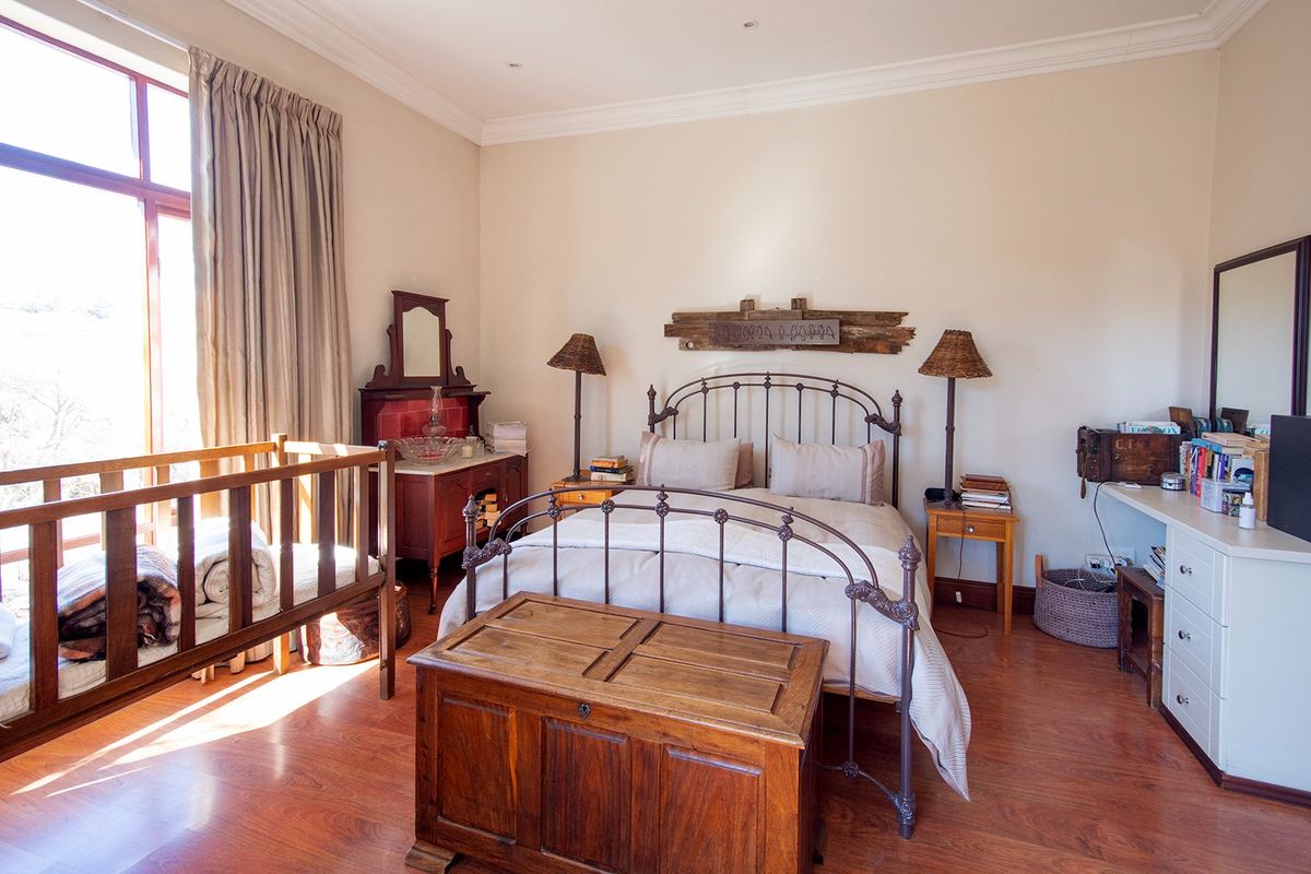 A spacious bedroom featuring warm-toned laminate flooring, large windows with natural light, and classic crown molding.
