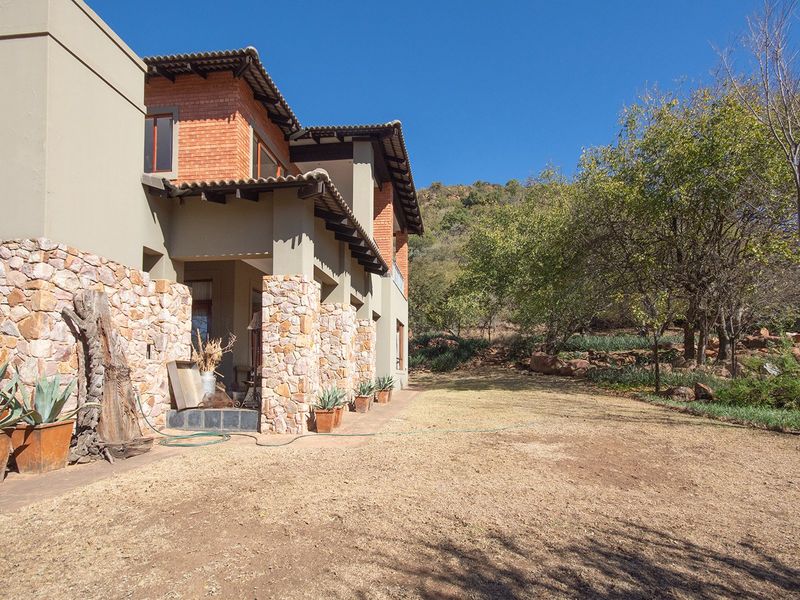 Rear view of the house featuring stone-clad pillars, brick accents, tiled roof, and a spacious garden area with mature trees.