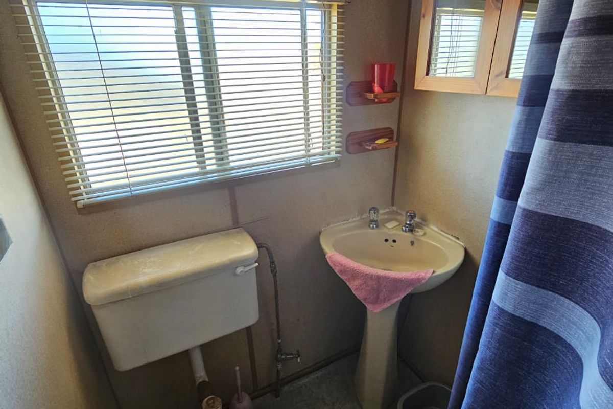 A compact bathroom featuring a pedestal sink, toilet, and shower area with dated wall finishes and functional fixtures.