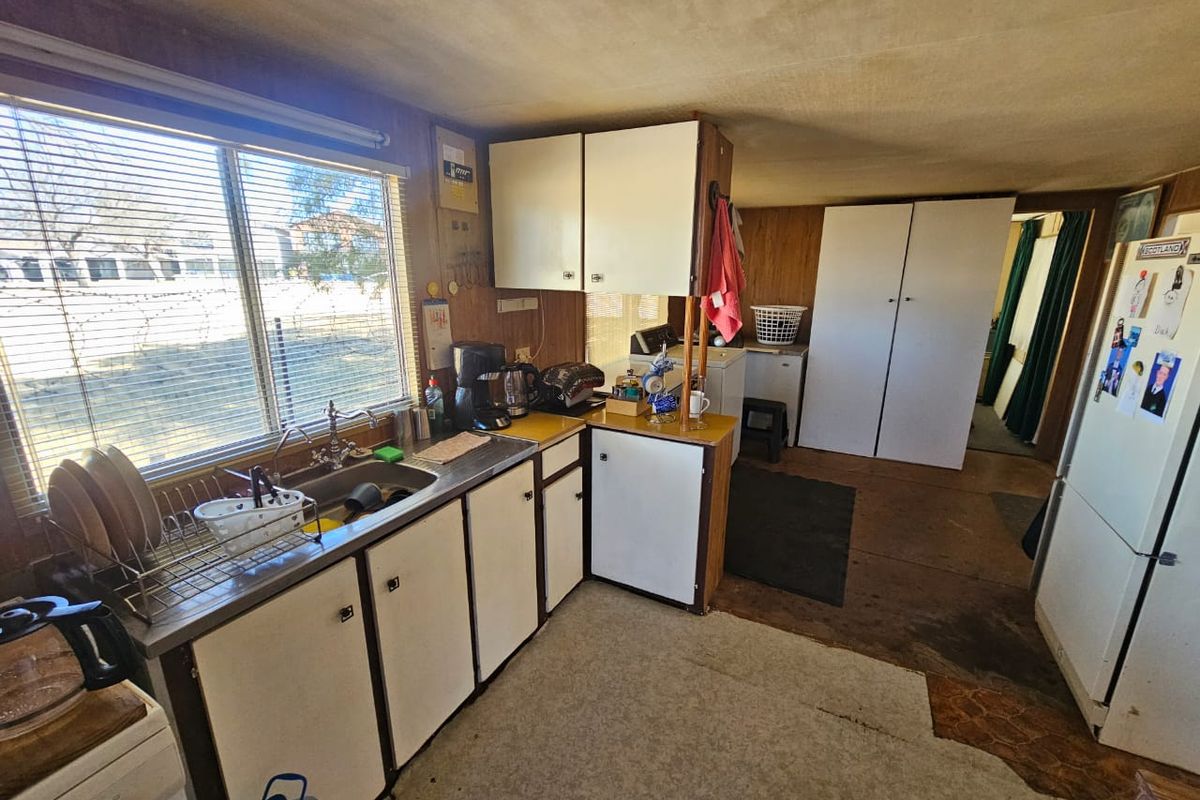 A dated kitchen area featuring original cabinetry, a stainless steel sink, and vinyl flooring, offering significant potential for a modern renovation.