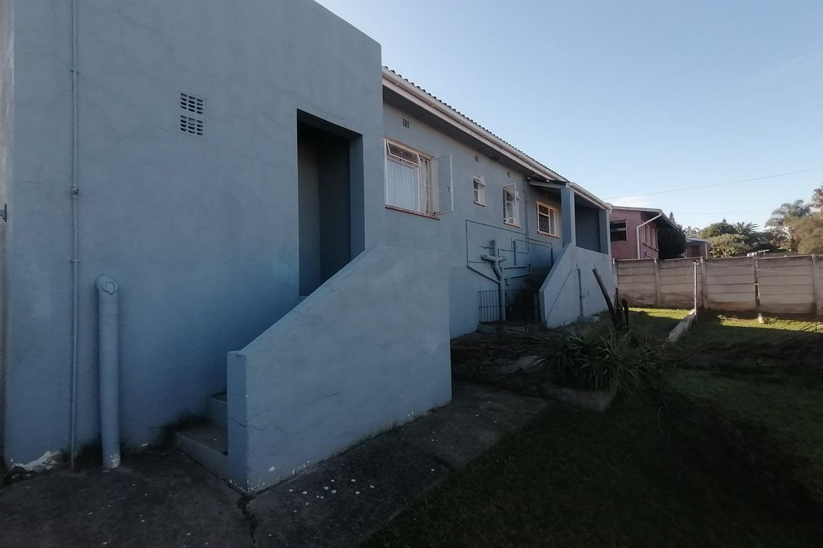 Rear exterior view of the property featuring a concrete staircase, exposed plumbing, and a small garden area with a perimeter boundary wall.