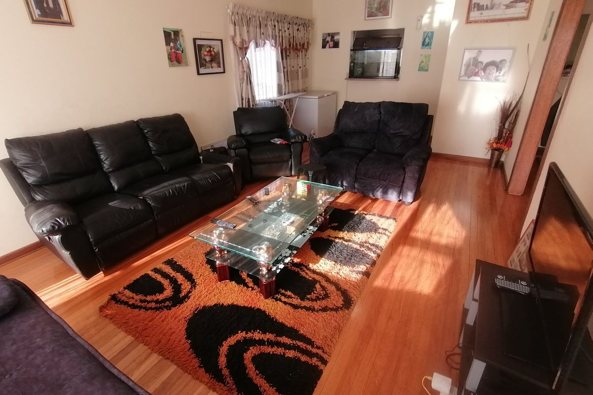 A living room featuring polished wooden flooring and a window with curtain rails.