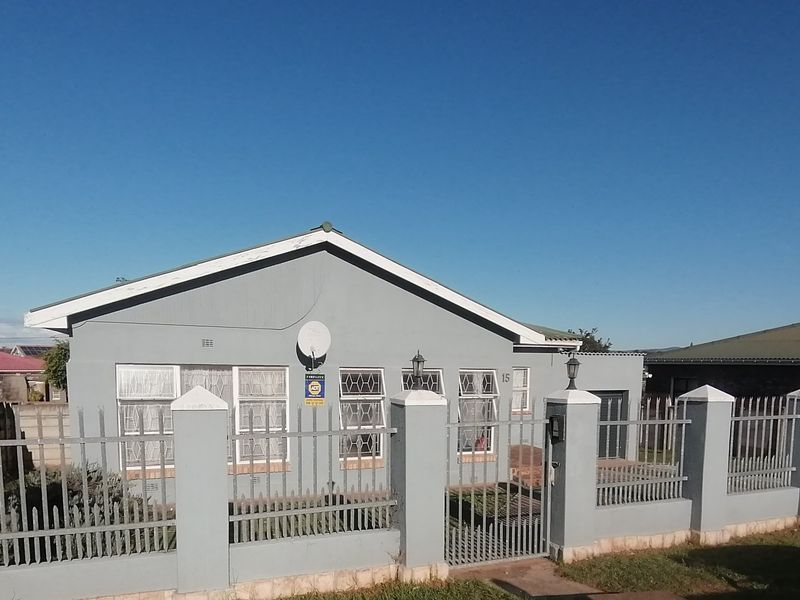 Front view of a single-story house featuring a secure perimeter wall with metal fencing, satellite dish, and paved entrance area.
