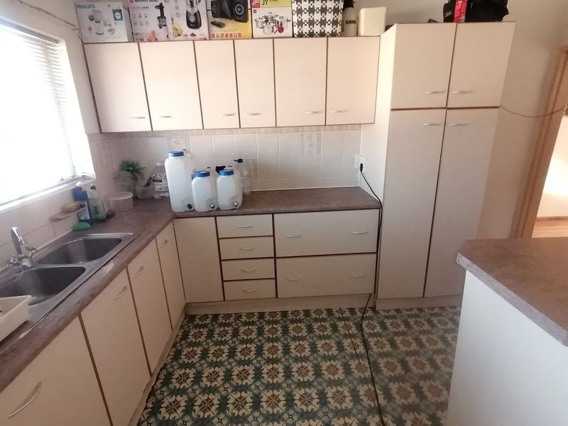 A functional kitchen featuring laminate countertops, double basin sink, tiled backsplash, and ample built-in cabinetry with a tall pantry unit.