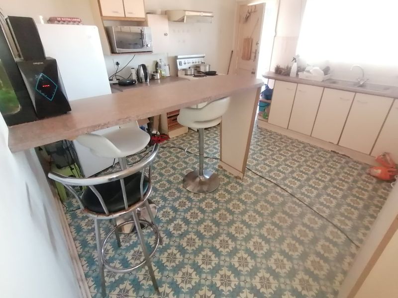 A dated kitchen featuring a breakfast bar, built-in cabinetry, and patterned floor tiles, offering a functional layout with potential for modernization.