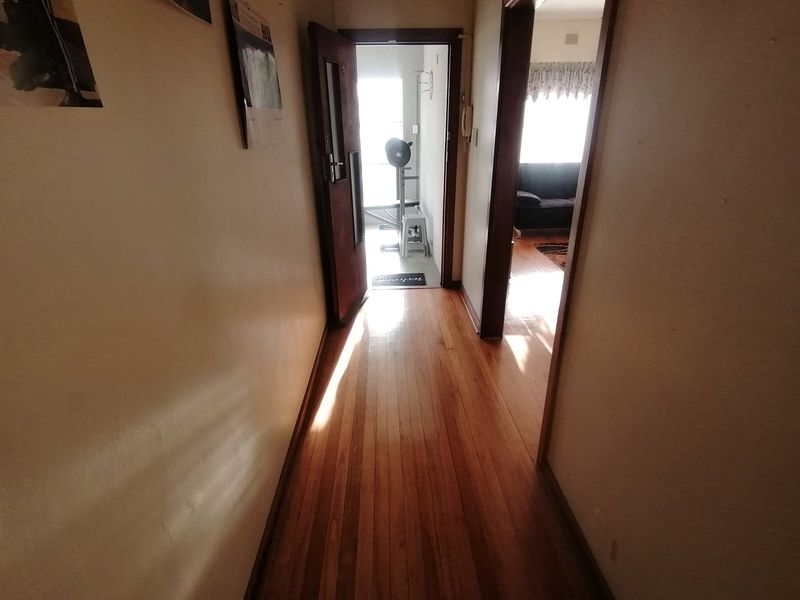 A hallway featuring polished timber flooring, providing access to adjacent rooms and an exterior entrance.