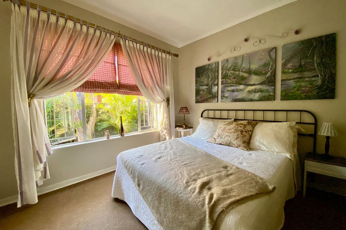 A cozy bedroom featuring carpeted flooring and a large window with security bars, offering a view of the garden.