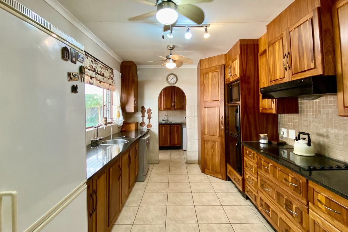 A functional kitchen featuring extensive wooden cabinetry, granite countertops, built-in oven, extractor fan, and ceramic tile flooring with a separate scullery area.