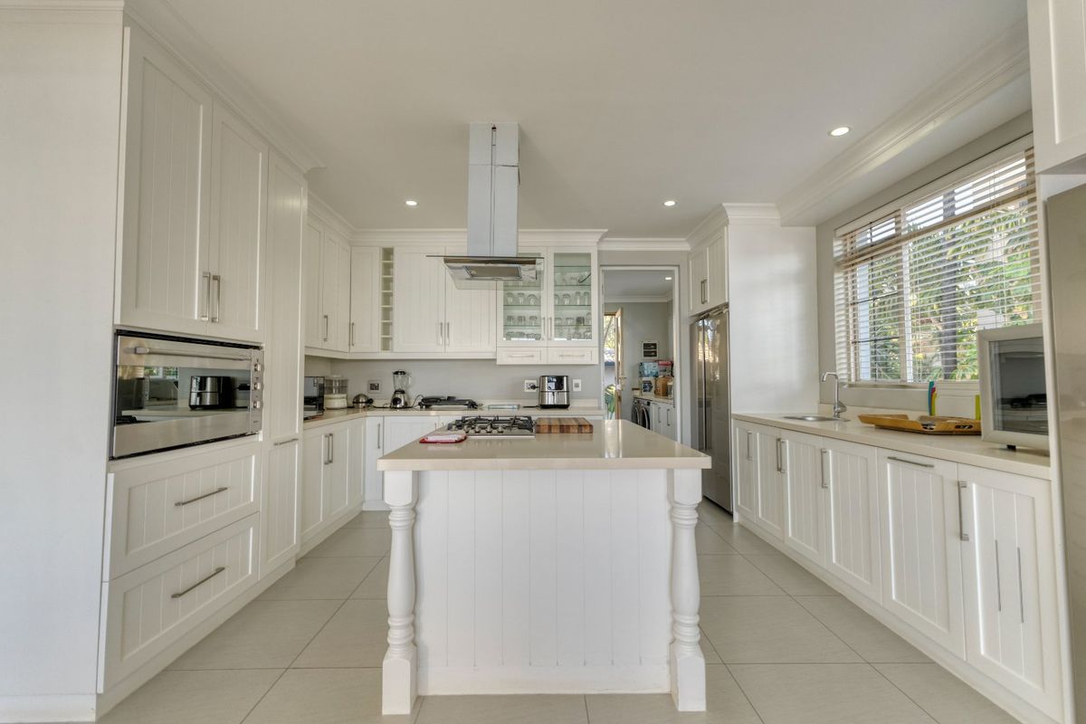 A bright, modern kitchen featuring white cabinetry, a central island with a gas cooktop, stainless steel appliances, and tiled flooring.