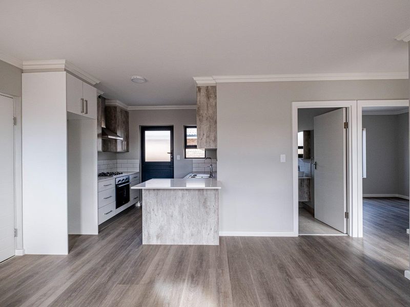 Modern open-plan kitchen featuring stone-look cabinetry, integrated oven and hob, and sleek countertops, seamlessly flowing into the adjacent living and hallway areas.